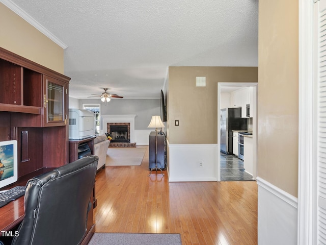 interior space with a ceiling fan, a textured ceiling, light wood-style flooring, and a fireplace