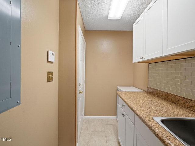 kitchen with electric panel, a textured ceiling, white cabinets, light countertops, and decorative backsplash