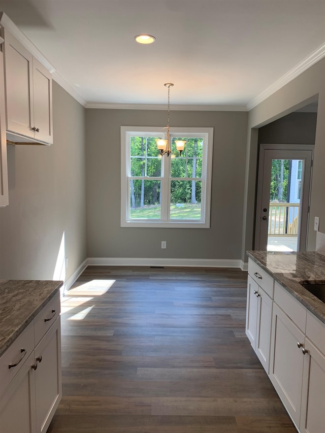 unfurnished dining area with a wealth of natural light, dark hardwood / wood-style floors, a notable chandelier, and ornamental molding