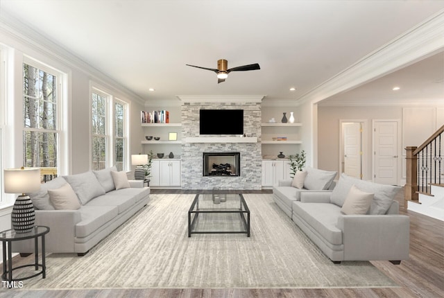 living room featuring built in shelves, wood finished floors, stairway, a fireplace, and crown molding