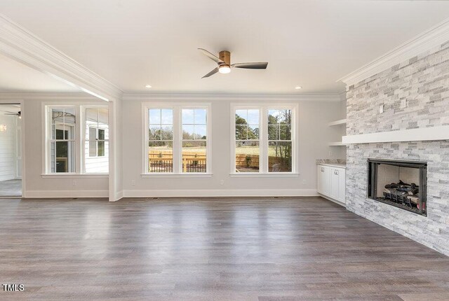 unfurnished living room featuring dark hardwood / wood-style floors, ceiling fan, a stone fireplace, and crown molding