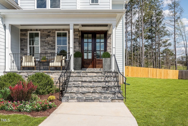 view of exterior entry with stone siding, french doors, a yard, and fence