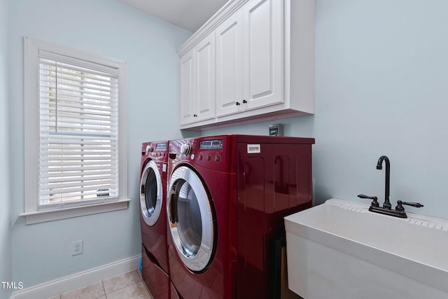 clothes washing area featuring light tile patterned floors, a sink, baseboards, washer and dryer, and cabinet space