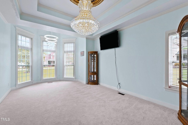 spare room with ornamental molding, a tray ceiling, a healthy amount of sunlight, and a notable chandelier