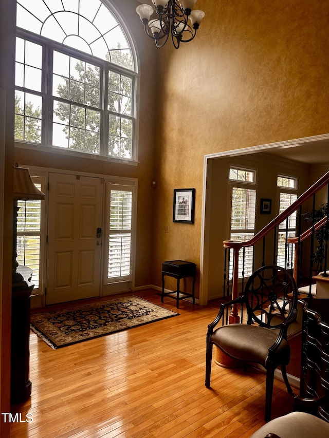 foyer entrance with a towering ceiling, wood-type flooring, and an inviting chandelier