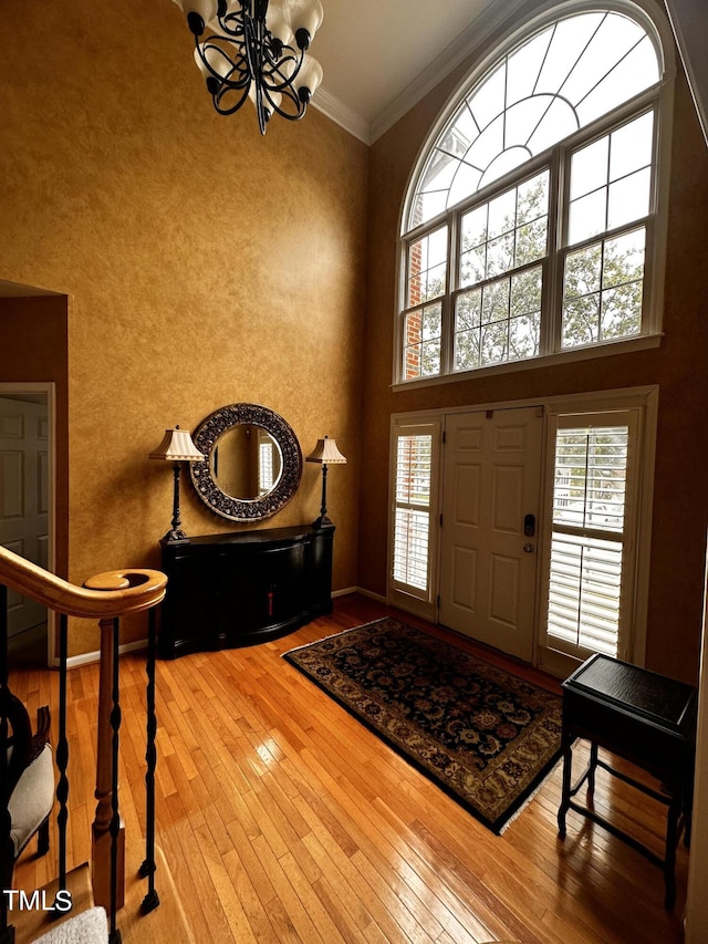 entrance foyer featuring a towering ceiling, hardwood / wood-style flooring, crown molding, and a healthy amount of sunlight