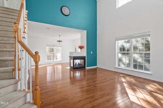 unfurnished living room featuring wood-type flooring, a towering ceiling, a multi sided fireplace, and stairs