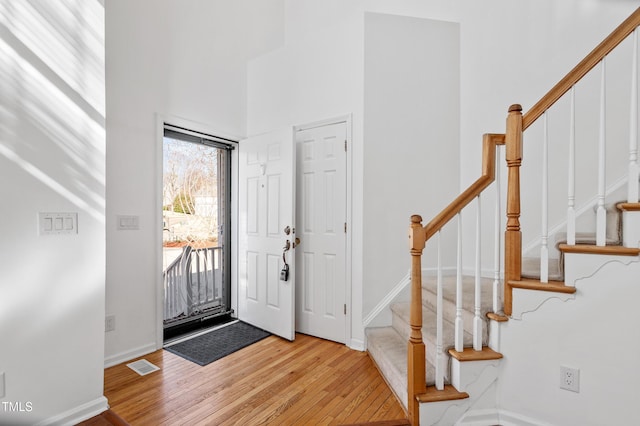 foyer entrance with baseboards, visible vents, a towering ceiling, wood finished floors, and stairs