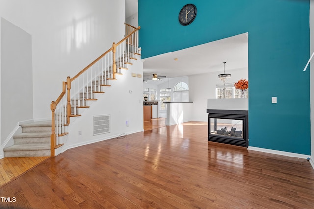 unfurnished living room featuring visible vents, baseboards, a towering ceiling, wood-type flooring, and stairway