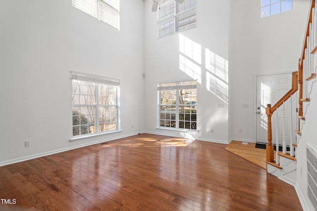 unfurnished living room featuring a healthy amount of sunlight, hardwood / wood-style flooring, baseboards, and stairway