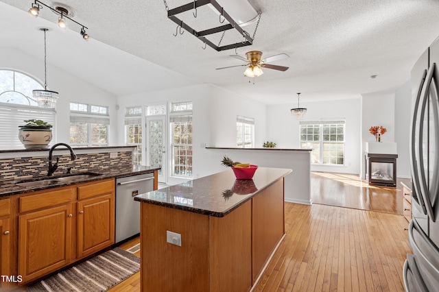 kitchen with lofted ceiling, light wood-style flooring, a kitchen island, a sink, and appliances with stainless steel finishes