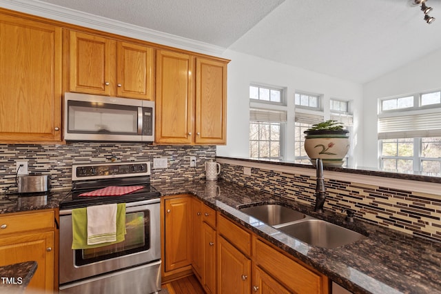 kitchen with appliances with stainless steel finishes, brown cabinetry, dark stone countertops, and a sink