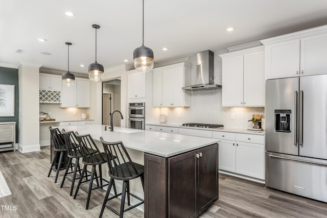 kitchen featuring white cabinets, an island with sink, wall chimney exhaust hood, light hardwood / wood-style flooring, and appliances with stainless steel finishes