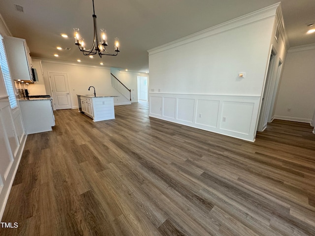 unfurnished living room featuring dark hardwood / wood-style floors, sink, an inviting chandelier, and ornamental molding