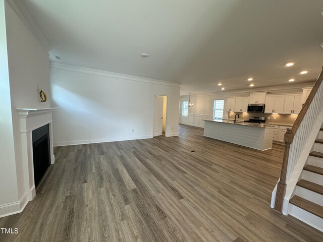 unfurnished living room with hardwood / wood-style floors, sink, and crown molding