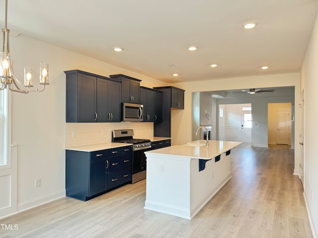 kitchen featuring decorative backsplash, an island with sink, light hardwood / wood-style floors, ceiling fan with notable chandelier, and stainless steel appliances