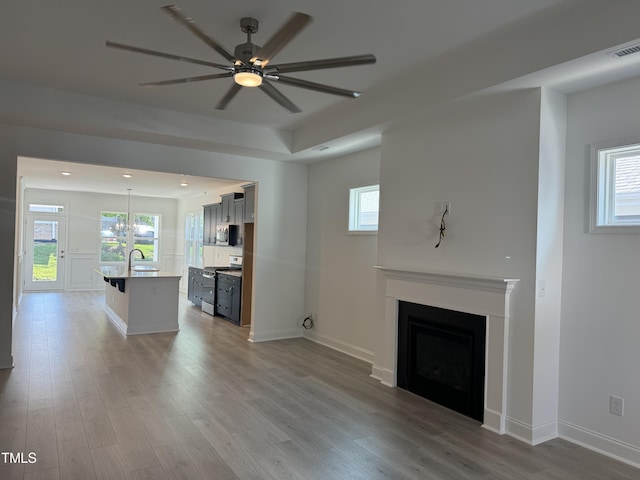 unfurnished living room with wood finished floors, visible vents, a fireplace, ceiling fan, and a sink