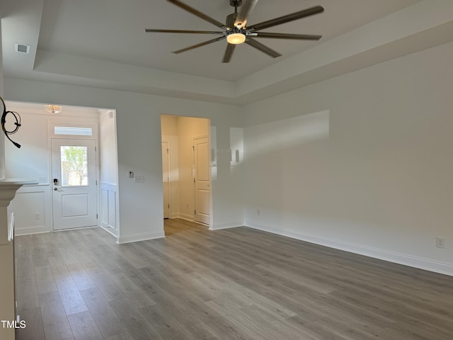 interior space featuring a raised ceiling, wood finished floors, a ceiling fan, and visible vents