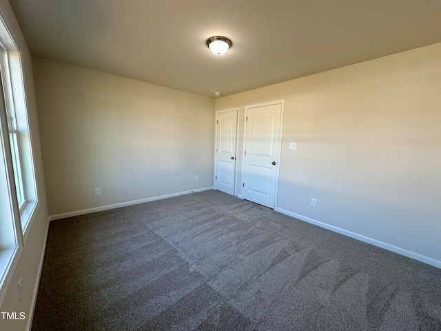 unfurnished room with plenty of natural light and dark colored carpet