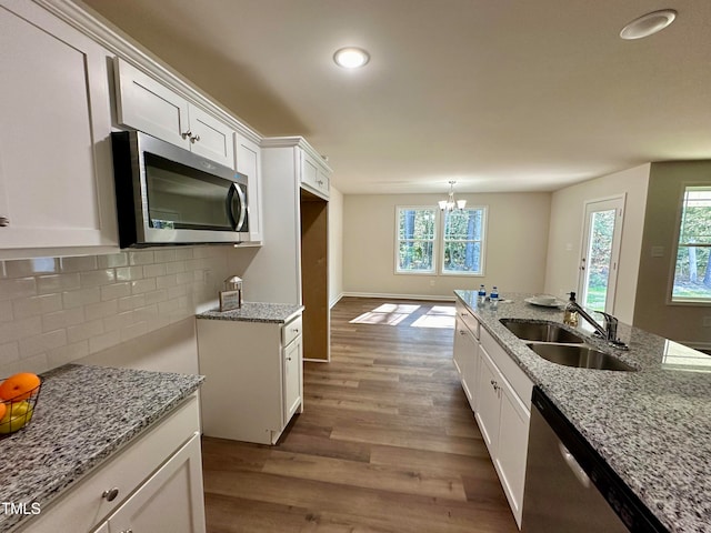 kitchen with appliances with stainless steel finishes, white cabinetry, sink, hardwood / wood-style flooring, and light stone counters