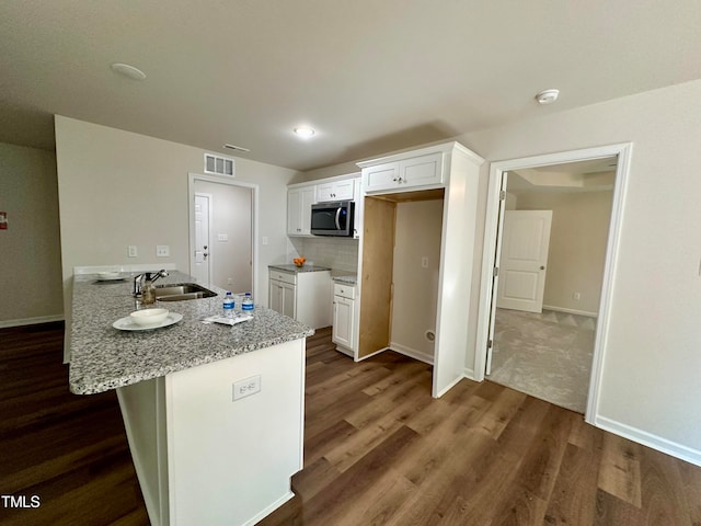 kitchen with light stone counters, sink, kitchen peninsula, and white cabinets