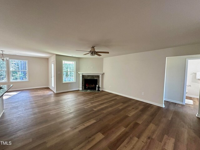 unfurnished living room featuring dark hardwood / wood-style floors, a premium fireplace, and ceiling fan with notable chandelier