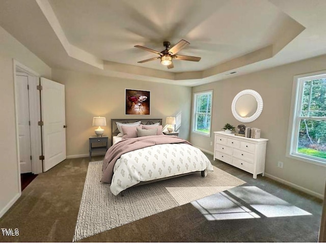 carpeted bedroom featuring a raised ceiling, ceiling fan, and multiple windows