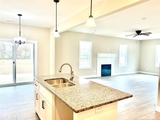 kitchen with an island with sink, light wood-type flooring, pendant lighting, light stone counters, and sink