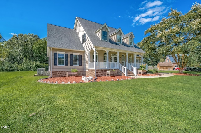 new england style home with central AC unit, a porch, roof with shingles, and a front yard