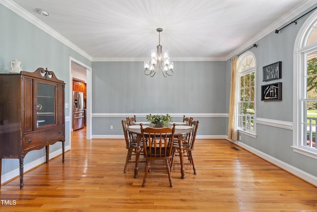 dining space featuring light wood finished floors, visible vents, baseboards, crown molding, and a notable chandelier