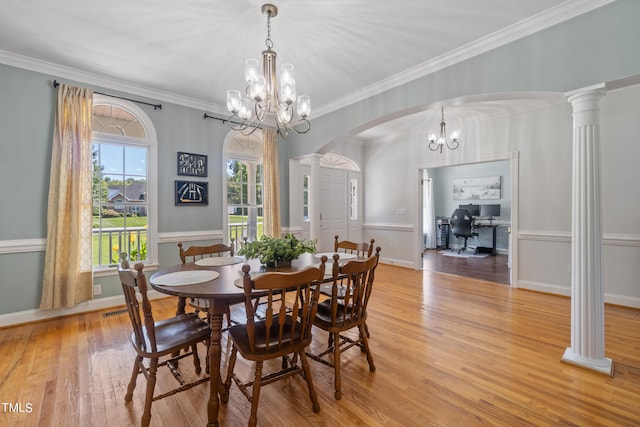 dining room with arched walkways, crown molding, light wood finished floors, and ornate columns