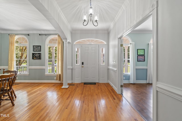 foyer entrance featuring light wood-style floors, decorative columns, a chandelier, and crown molding