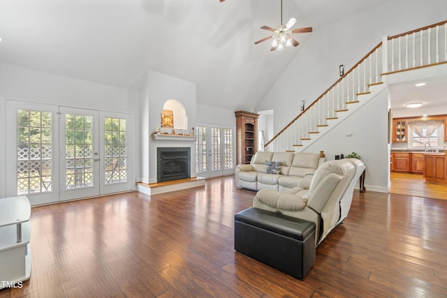 living room with dark wood-style flooring, french doors, a fireplace with raised hearth, high vaulted ceiling, and stairs