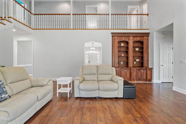 living area with arched walkways, dark wood-style flooring, a notable chandelier, a towering ceiling, and baseboards