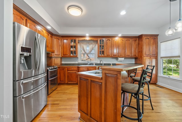 kitchen with brown cabinets, stainless steel appliances, light wood-style floors, glass insert cabinets, and a sink