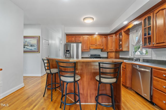 kitchen featuring light wood finished floors, stainless steel appliances, glass insert cabinets, a sink, and a kitchen bar