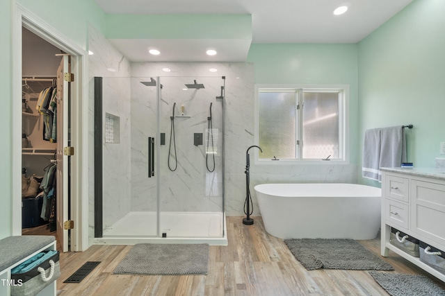 bathroom featuring a walk in closet, a marble finish shower, a freestanding bath, vanity, and wood finished floors