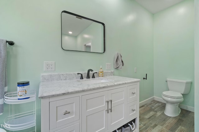 bathroom featuring toilet, baseboards, wood finished floors, and vanity