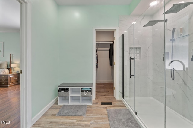 full bath with baseboards, a spacious closet, a marble finish shower, and wood finished floors