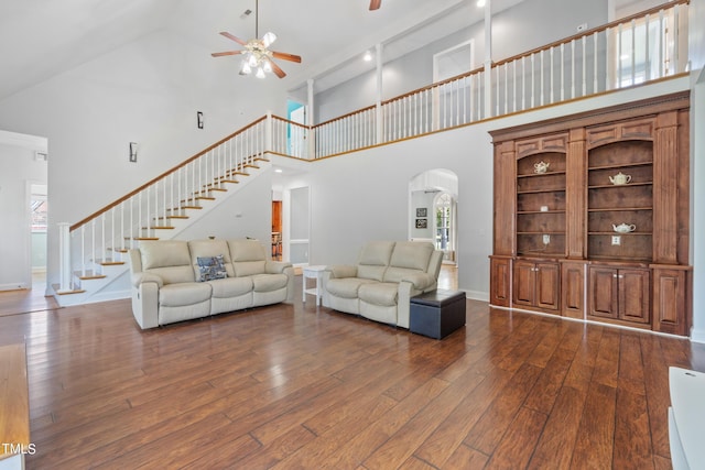 living area with ceiling fan, arched walkways, baseboards, stairway, and dark wood-style floors