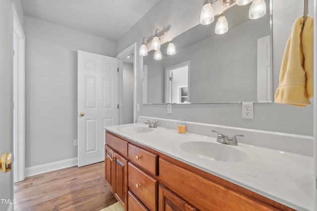 full bathroom with double vanity, baseboards, a sink, and wood finished floors