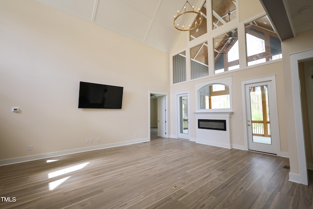 unfurnished living room featuring high vaulted ceiling, an inviting chandelier, and hardwood / wood-style flooring