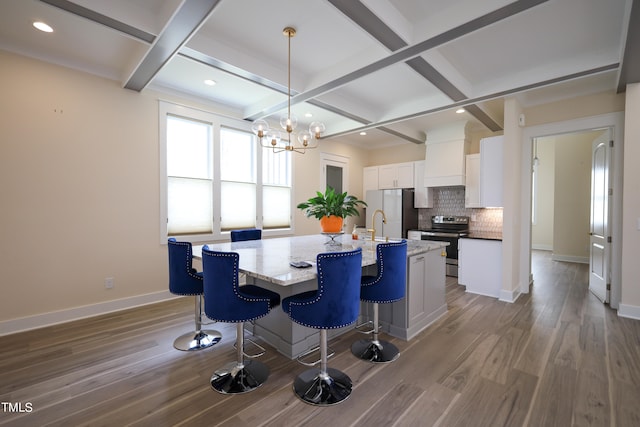 dining space with coffered ceiling, beamed ceiling, light hardwood / wood-style floors, and a chandelier