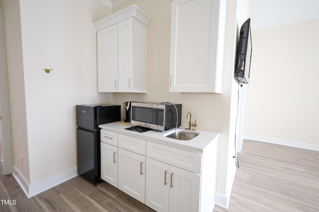 kitchen with sink, black refrigerator, light hardwood / wood-style floors, and white cabinetry