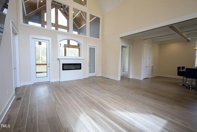 unfurnished living room with beam ceiling, hardwood / wood-style floors, and a high ceiling