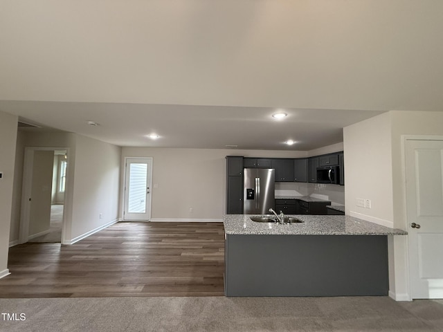 kitchen with kitchen peninsula, stainless steel fridge, light stone countertops, dark wood-type flooring, and sink