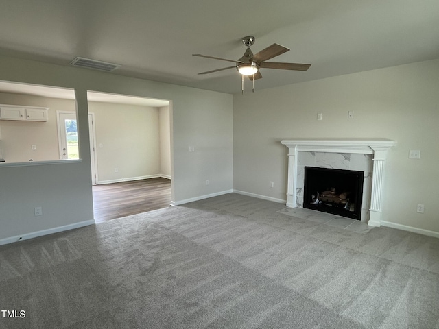 unfurnished living room featuring carpet flooring, a high end fireplace, baseboards, visible vents, and ceiling fan