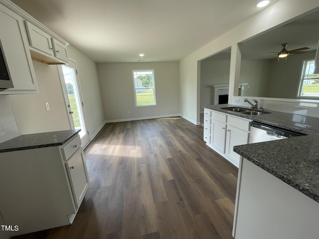kitchen featuring white cabinetry, stainless steel dishwasher, dark stone counters, a sink, and dark wood-style floors