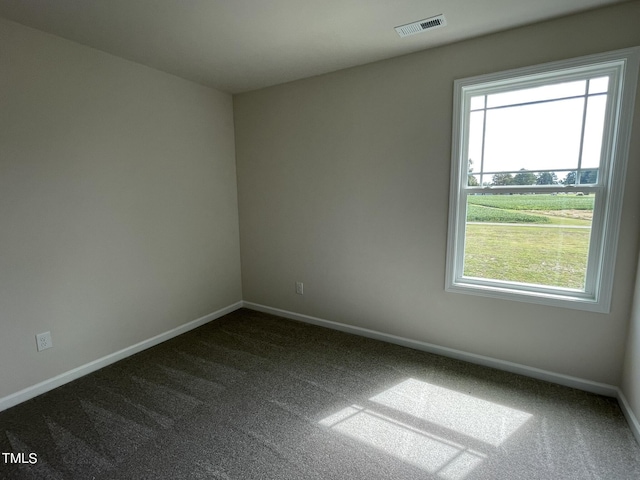 spare room featuring baseboards, visible vents, and dark carpet