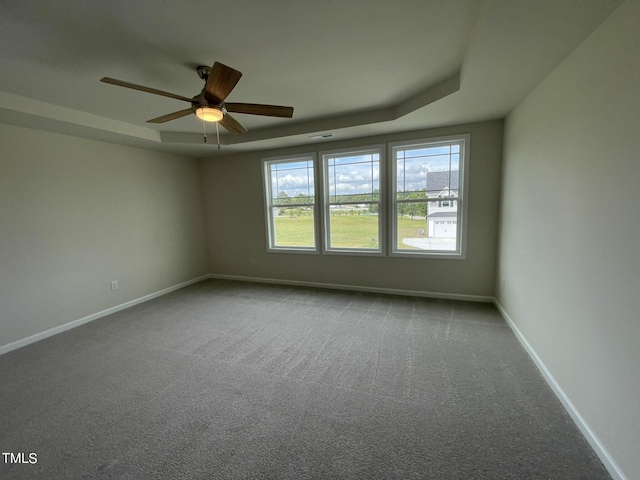 empty room featuring a ceiling fan, a raised ceiling, carpet, and baseboards